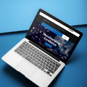 A MacBook Pro open on a two-color surface displaying the custom-designed, dark-themed GST Manufacturing website home page.