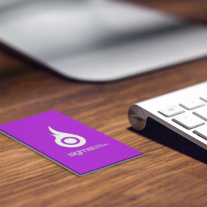 Two minimalist Sigma Payments business cards with a bright purple logo and clean typography, displayed on a textured wooden background next to a laptop.