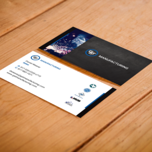Two custom-designed GST Manufacturing business cards angled on a rustic dark wood surface, showcasing a clean white layout with a blue and black geometric logo.