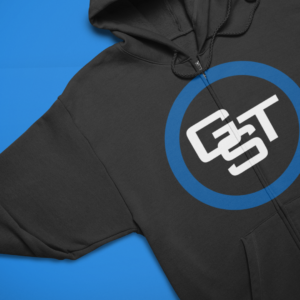 A close-up studio shot of a dark charcoal grey hoodie featuring the custom GST logo embroidered in clean white stitching inside a blue circle on the left chest.